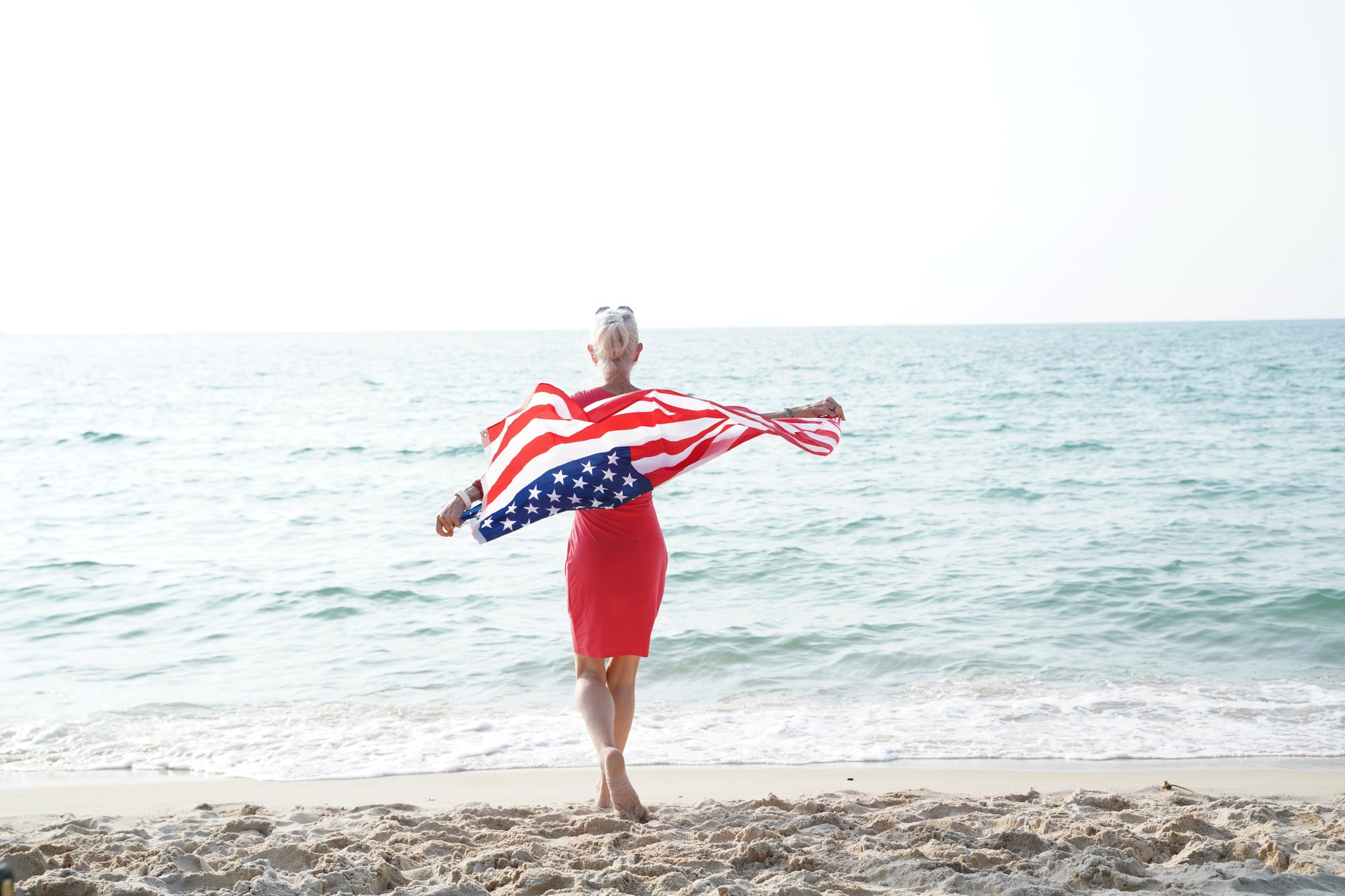 Woman holding US flag enjoying time at the beach.